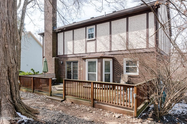 rear view of house with brick siding, a wooden deck, and stucco siding