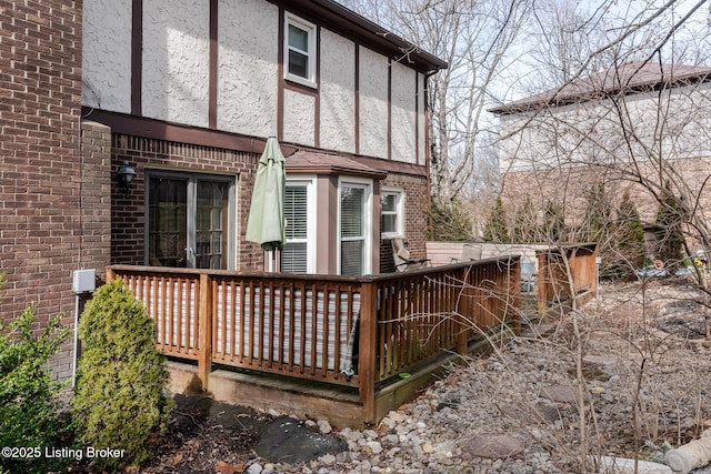 back of property with brick siding, a wooden deck, and stucco siding