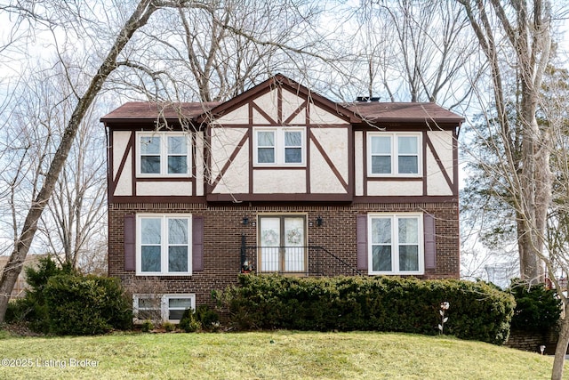 tudor home with brick siding, a front lawn, and stucco siding