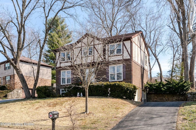 tudor house featuring brick siding, aphalt driveway, an attached garage, a front lawn, and stucco siding