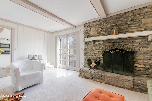 carpeted living room featuring a stone fireplace and beamed ceiling