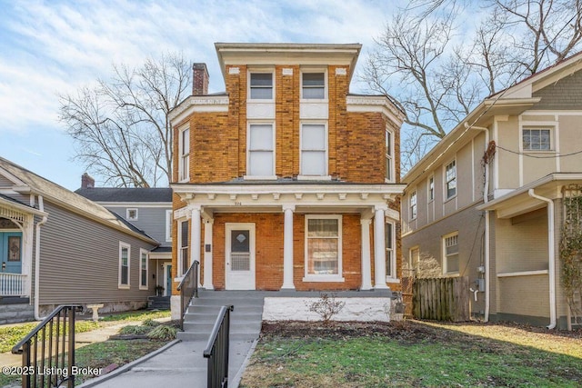 view of front of home with brick siding, covered porch, a chimney, and fence