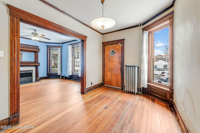 interior space featuring light wood-type flooring, a fireplace with flush hearth, ornamental molding, radiator heating unit, and baseboards