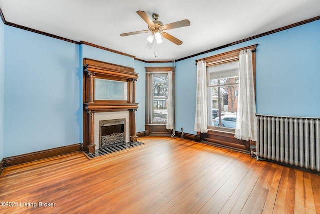 unfurnished living room featuring hardwood / wood-style floors, radiator, baseboards, a fireplace with flush hearth, and crown molding