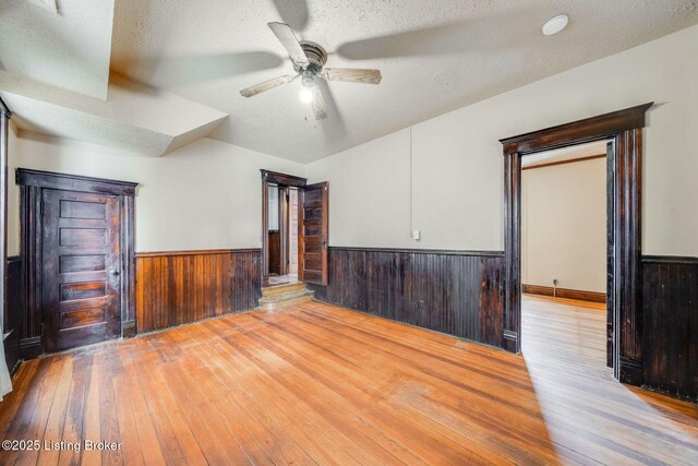 unfurnished room with a textured ceiling, ceiling fan, hardwood / wood-style floors, and wainscoting