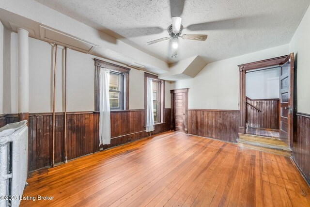 empty room featuring wooden walls, wainscoting, a textured ceiling, and wood-type flooring