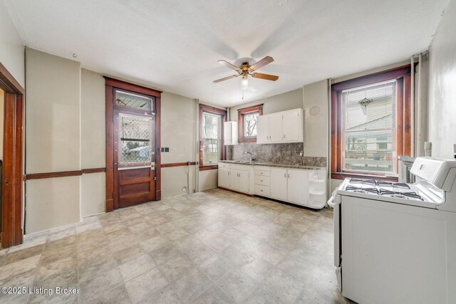 kitchen featuring a sink, gas range gas stove, backsplash, white cabinetry, and ceiling fan