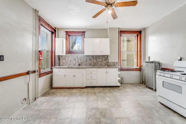 kitchen featuring white range with gas stovetop, ceiling fan, decorative backsplash, a sink, and white cabinetry