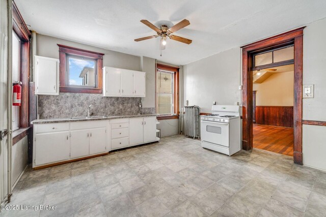 kitchen with light floors, white gas range oven, wainscoting, white cabinets, and a sink