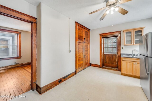 kitchen with glass insert cabinets, baseboards, light floors, freestanding refrigerator, and a sink