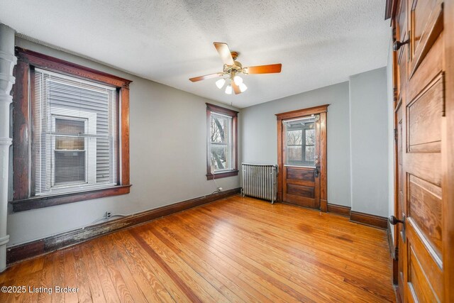 spare room with baseboards, light wood-type flooring, radiator heating unit, a textured ceiling, and a ceiling fan