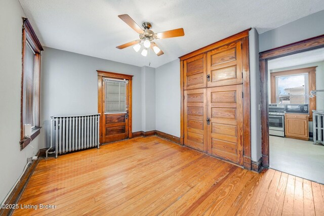 unfurnished bedroom featuring a ceiling fan, radiator, light wood-style floors, and baseboards