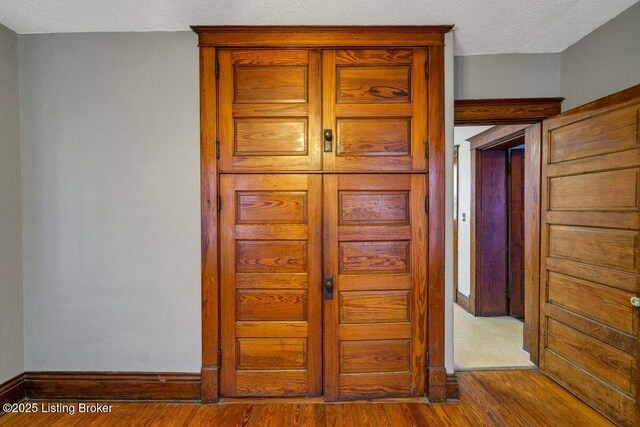 corridor with a textured ceiling, baseboards, and wood finished floors