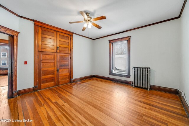 unfurnished bedroom featuring radiator, crown molding, baseboards, and hardwood / wood-style floors