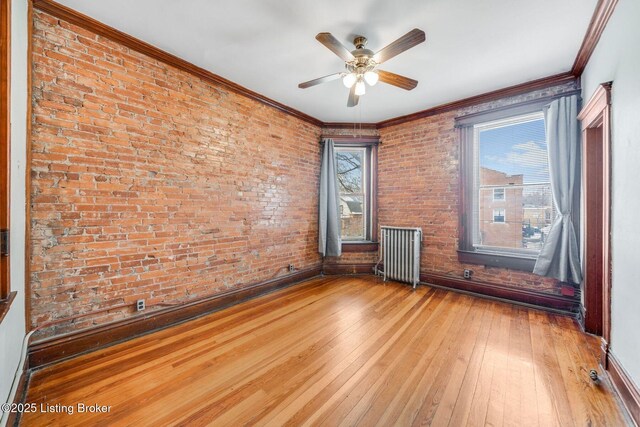 spare room featuring ornamental molding, a ceiling fan, radiator heating unit, wood-type flooring, and brick wall