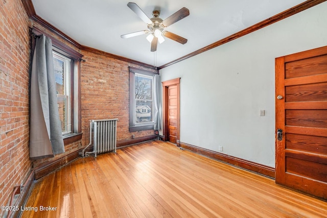 unfurnished room with brick wall, radiator, baseboards, ornamental molding, and hardwood / wood-style flooring