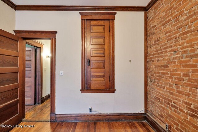 unfurnished room with brick wall, crown molding, baseboards, and hardwood / wood-style floors