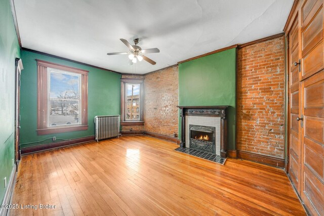 unfurnished living room featuring ornamental molding, wood-type flooring, radiator, brick wall, and a fireplace