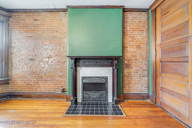 unfurnished living room featuring wood finished floors, baseboards, brick wall, a fireplace, and ornamental molding