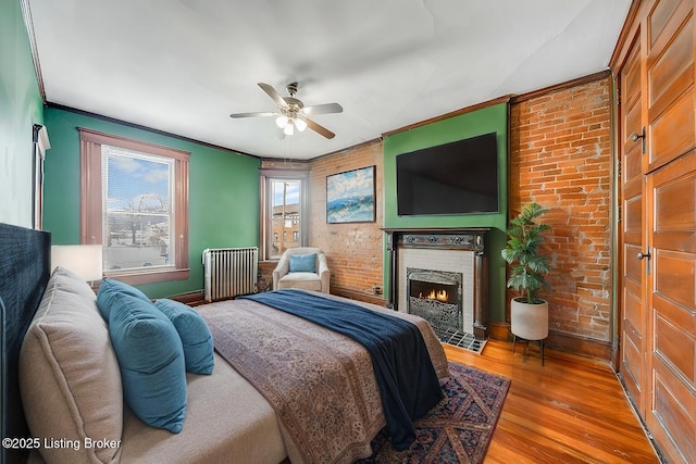 bedroom featuring a fireplace with flush hearth, ornamental molding, wood finished floors, radiator, and brick wall