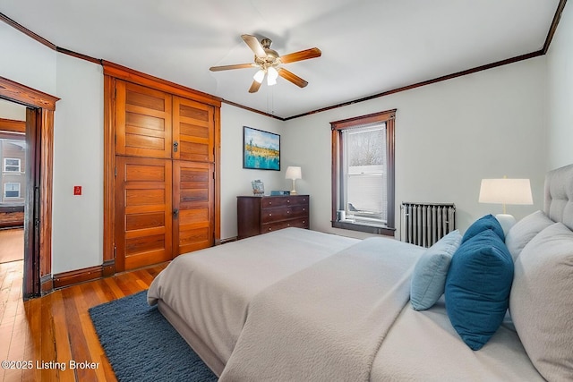 bedroom with radiator, crown molding, baseboards, hardwood / wood-style floors, and a ceiling fan