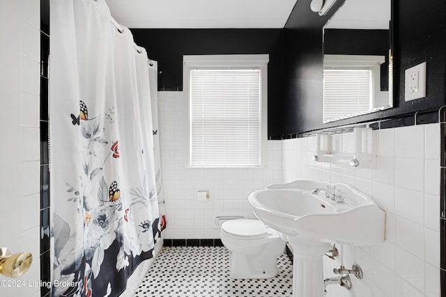 bathroom featuring a shower with curtain, toilet, tile patterned flooring, and tile walls