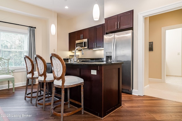 kitchen featuring dark wood-type flooring, a breakfast bar area, hanging light fixtures, appliances with stainless steel finishes, and a kitchen island with sink