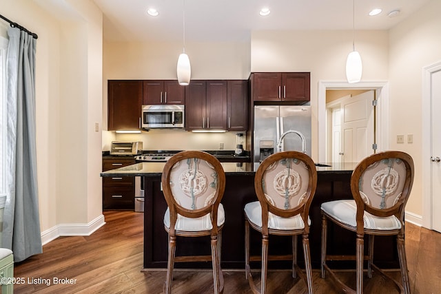 kitchen featuring an island with sink, appliances with stainless steel finishes, a breakfast bar area, and decorative light fixtures