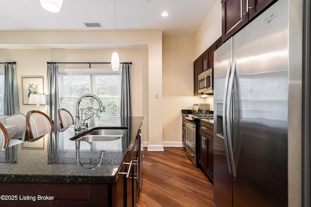 kitchen with sink, hanging light fixtures, dark stone countertops, an island with sink, and stainless steel appliances