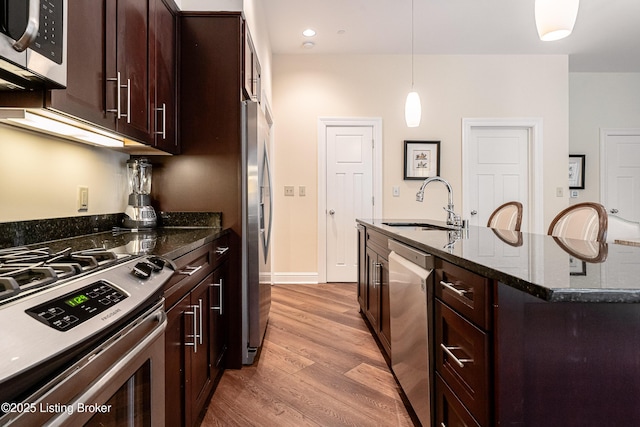 kitchen with sink, decorative light fixtures, light wood-type flooring, appliances with stainless steel finishes, and dark stone counters