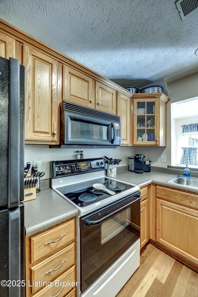 kitchen featuring a textured ceiling, sink, light hardwood / wood-style flooring, and black appliances