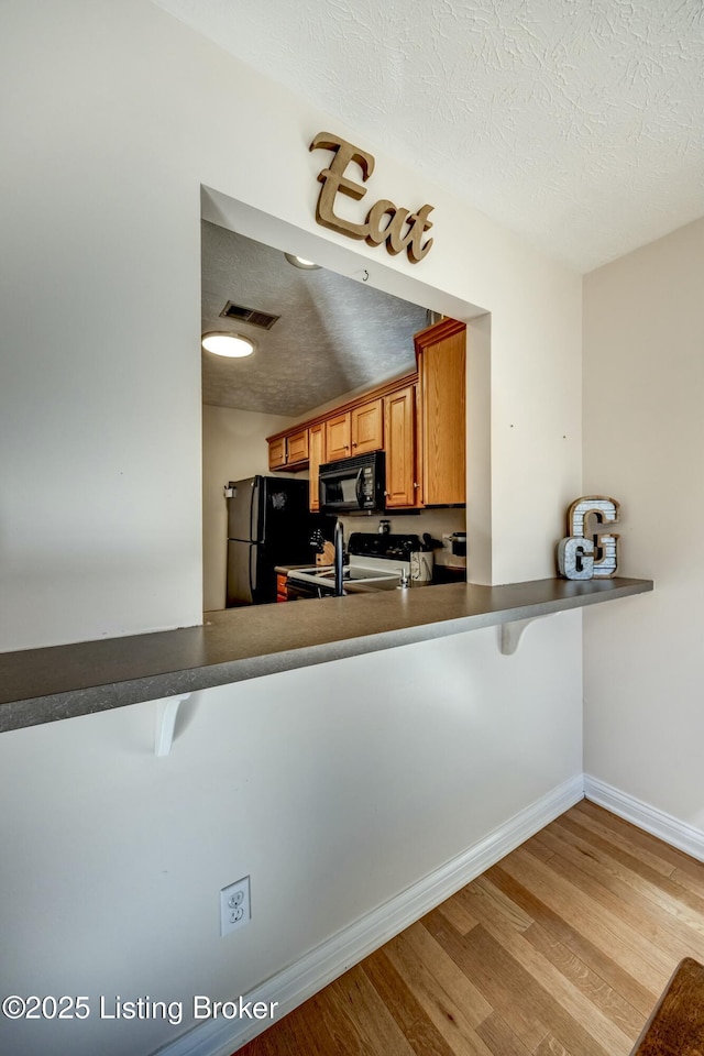 kitchen featuring a kitchen bar, light wood-type flooring, a textured ceiling, and black appliances