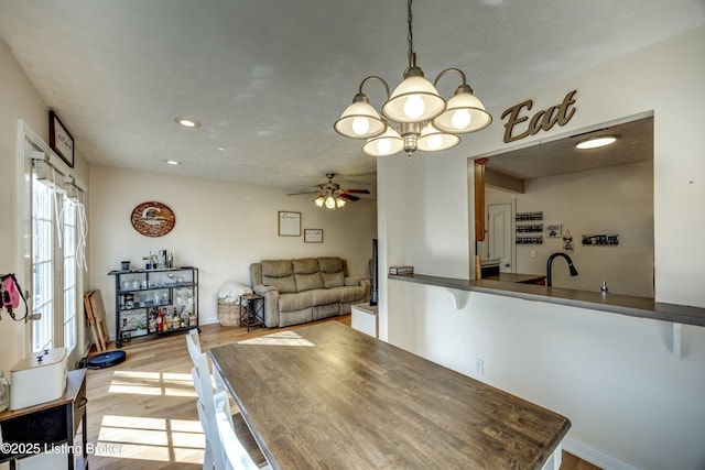 dining room featuring ceiling fan with notable chandelier, sink, and light hardwood / wood-style floors