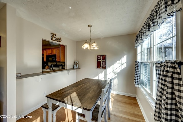 dining room with an inviting chandelier, sink, light hardwood / wood-style floors, and a textured ceiling