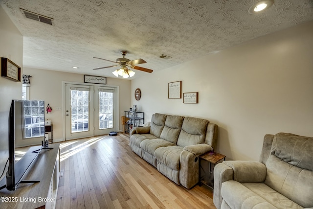 living room with ceiling fan, a textured ceiling, and light wood-type flooring