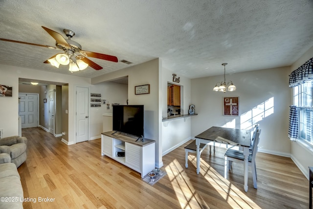 living room with ceiling fan with notable chandelier, a textured ceiling, and light wood-type flooring