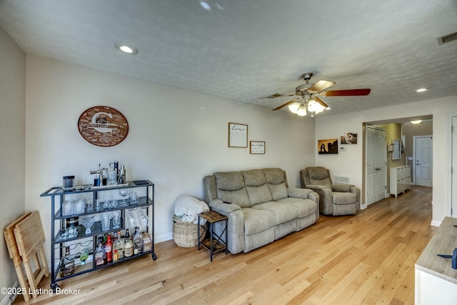 living room with ceiling fan, light hardwood / wood-style floors, and a textured ceiling