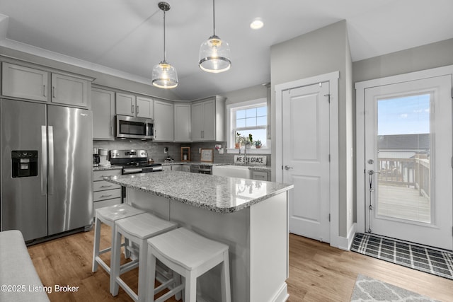 kitchen featuring appliances with stainless steel finishes, decorative backsplash, hanging light fixtures, light stone counters, and light hardwood / wood-style flooring