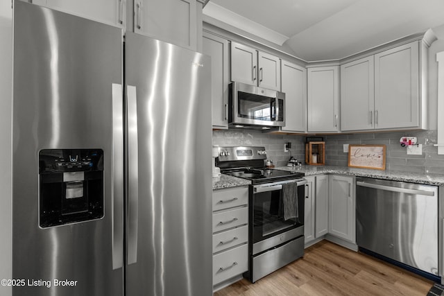 kitchen with appliances with stainless steel finishes, tasteful backsplash, lofted ceiling, light stone counters, and light wood-type flooring