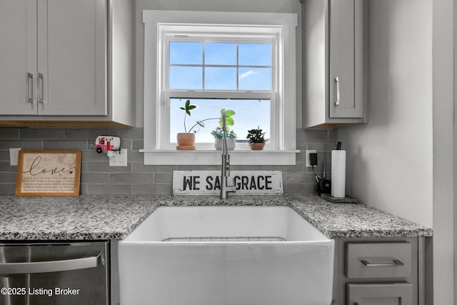 kitchen with sink, tasteful backsplash, stainless steel dishwasher, gray cabinets, and light stone countertops