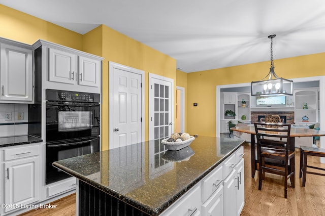 kitchen with dark stone countertops, double oven, a center island, and white cabinets