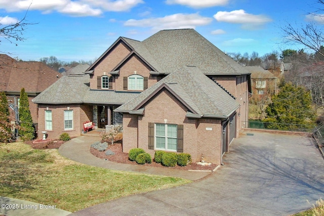 view of front facade featuring brick siding, driveway, and a shingled roof