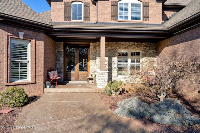 property entrance with brick siding, french doors, stone siding, and a shingled roof