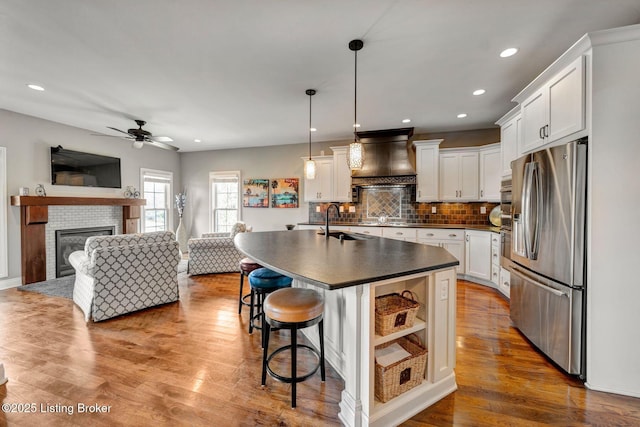 kitchen featuring dark countertops, open floor plan, custom range hood, stainless steel refrigerator with ice dispenser, and wood finished floors