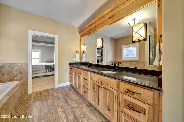 full bathroom featuring a sink, wood finished floors, double vanity, and tiled bath