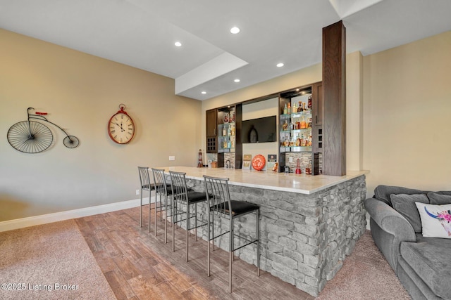 bar with a bar, recessed lighting, baseboards, and light wood-type flooring