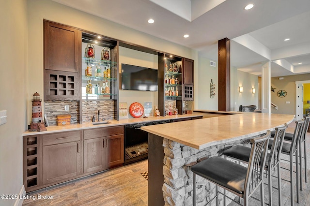 bar with wet bar, light wood-style flooring, recessed lighting, a sink, and backsplash