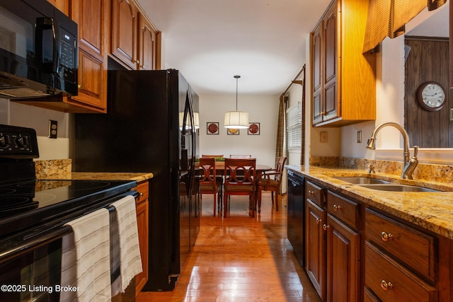 kitchen featuring sink, wood-type flooring, black appliances, light stone countertops, and decorative light fixtures