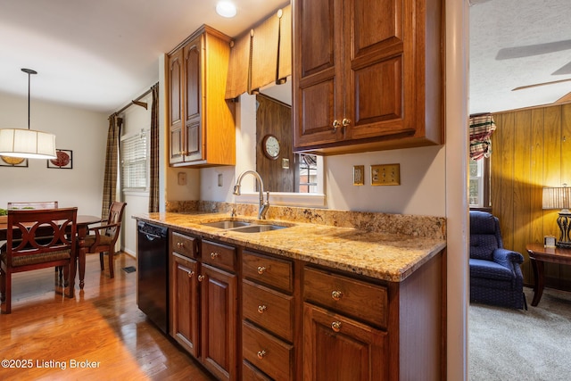 kitchen with sink, black dishwasher, light stone counters, wood-type flooring, and decorative light fixtures