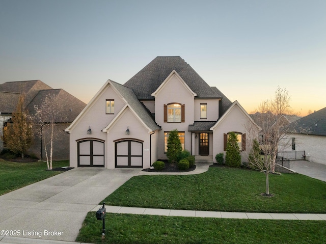 french provincial home with a garage, a front yard, driveway, and a shingled roof